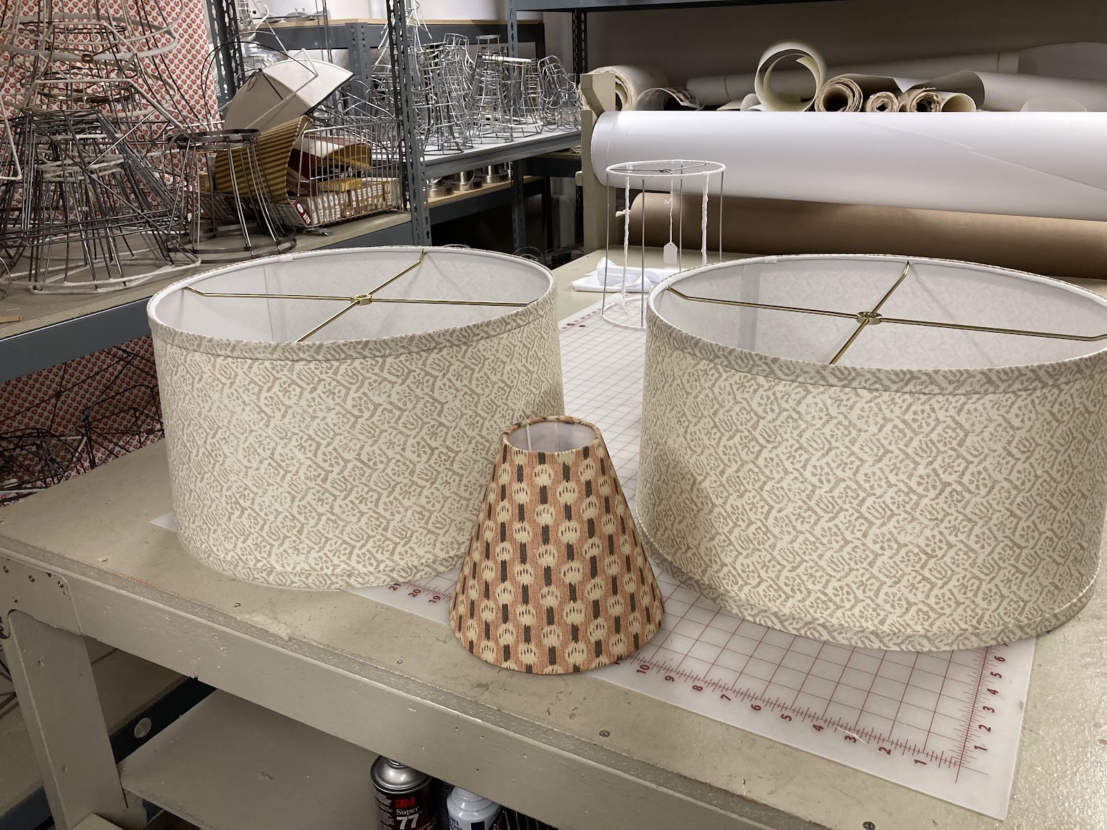 Custom drum lampshades in progress on the worktable in the Lili Marlene workroom, with wire frames and rolls of shade paper behind them
